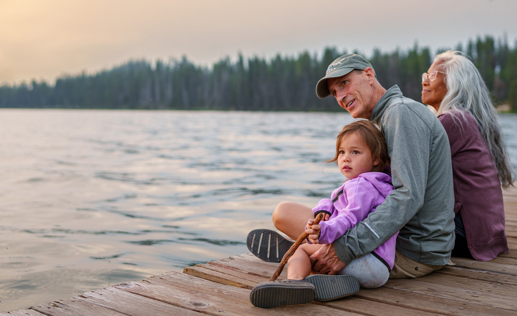 A family sit on a pontoon looking out across a lake with a pine forest in the distance